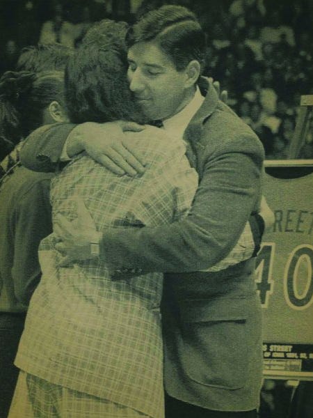 Iowa athletic director Bob Bowlsby hugs Patricia Street, mother of Chris, during pregame ceremony retiring Street's jersey. The easle at right holds the mounted jersey.