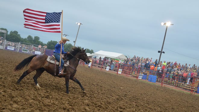 Brittany Bloom of Lisbon-based Sandburr Rodeo Productions carries the American flag during the National Anthem before the rodeo Friday night at the Johnson County 4-H Fairgrounds.