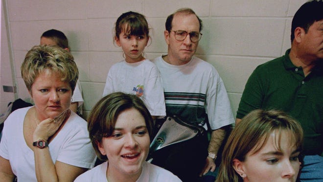 In this March 18, 1997 photo and with eight-year-old Mackenzie on his lap, Dan Gable watches 14-year-old daughter Molly compete at a swimming meet in Iowa City. His wife, Kathy, is at left, next to daughters Annie, 17 and Jenni, 19.