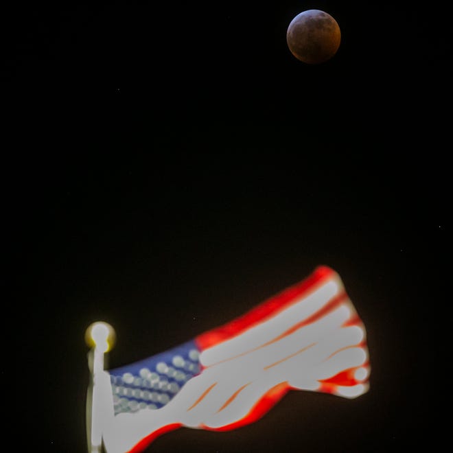 The super blood wolf moon eclipse is seen past an American flag on the Old Capitol Building on Sunday, Jan. 20, 2019, seen from the Pentacrest in Iowa City, Iowa.