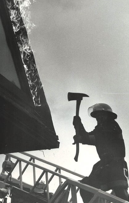 From 1983: A Des Moines firefighter uses his ax to strip wood trim from the burning roof of the Colonial Arms apartments on Grand Avenue.