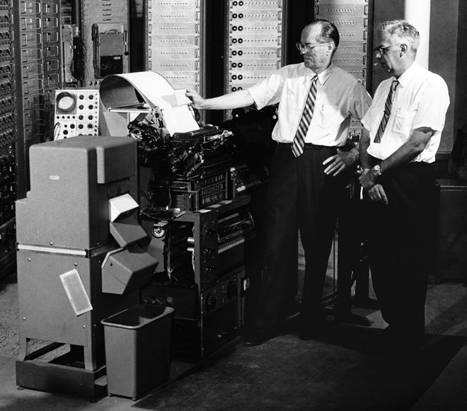 ACT CoFounders E.F. Lindquist and Ted McCarrel stand next to a scoring machine.